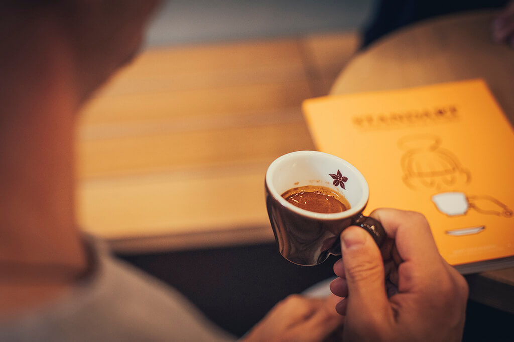 Man holding an espresso cup inside a coffee island store.