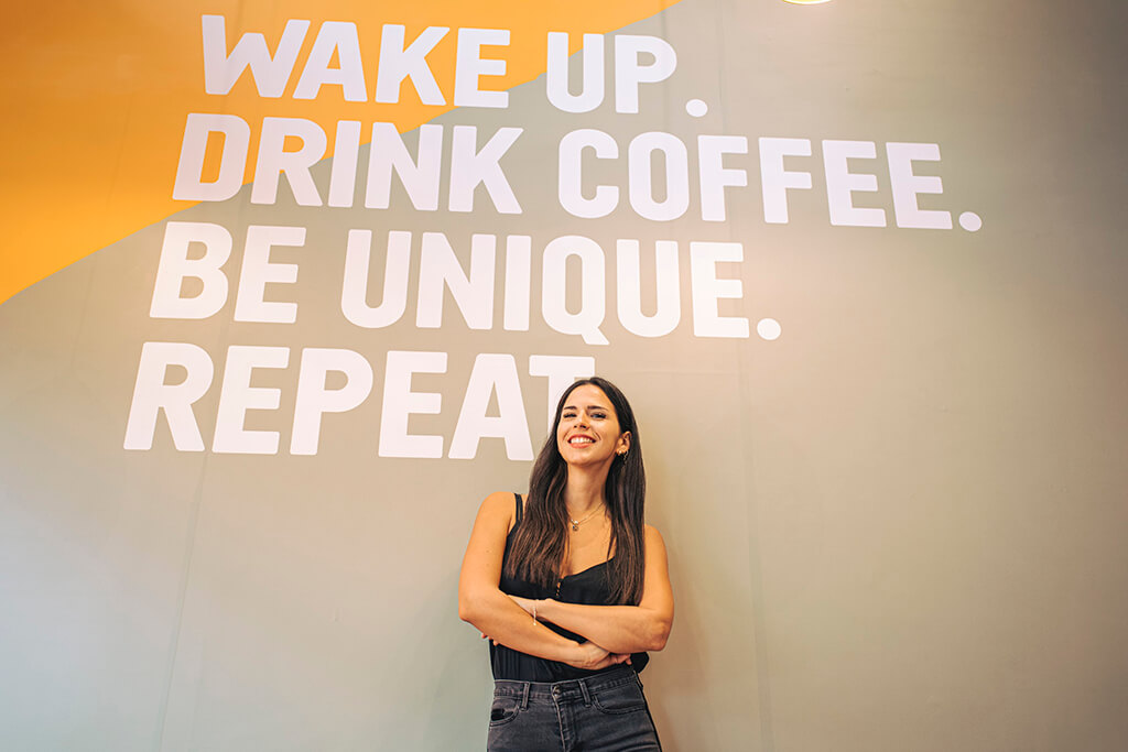 Woman standing below a wall-message inside a coffee island store.
