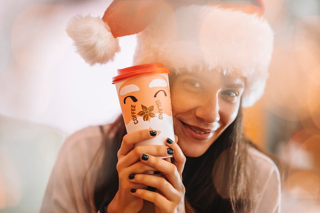 Happy woman holding her Coffee Island Santa Christmas cup