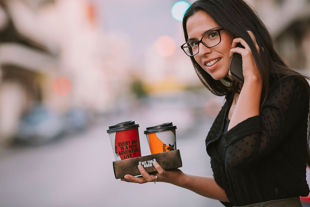 A woman, while speaking on her cellphone, holds two coffee island cups.